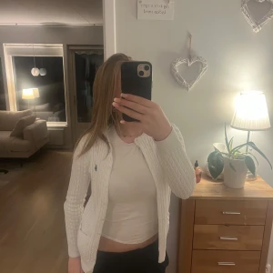 Vit stickad kofta från Ralph Lauren Sport - Säljer en superfin vit stickad kofta från Ralph Lauren Sport i storlek XS. Den har ett klassiskt kabelstickat mönster. Köpt i USA för ett tag sen men aldrig använd, dedär jah säljer( köpt för 2500kr)Perfekt för både vardag och fest! 🧶✨