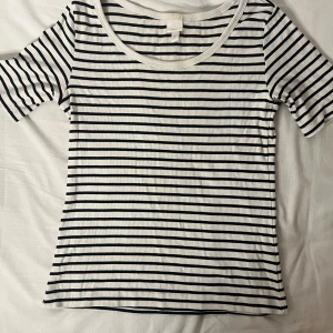 Randig t-shirt från H&M - Säljer en snygg randig t-shirt från H&M i svart och vit. Den är ribbad och har korta ärmar, perfekt för en avslappnad stil. Passar bra till både jeans och kjol. Perfekt för vår och sommar!