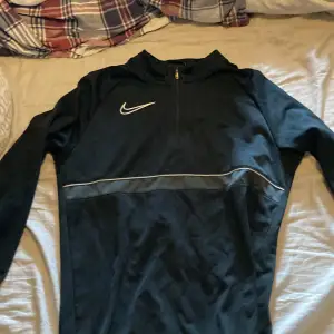 Säljer en svart långärmad tröja från Nike med Dri-FIT-teknologi. Perfekt för träning eller vardagsbruk. Tröjan har en dragkedja vid halsen och en vit Nike-logga på bröstet. Den är i bra skick och superbekväm att ha på sig. Passar perfekt för höst och vår!