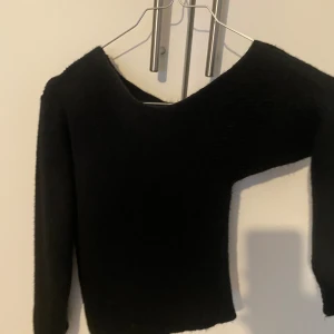 Svart stickad tröja - Säljer en mysig svart stickad tröja med långärmad,offsholder design. Perfekt för kyliga dagar och kan stylas både upp och ner. Tröjan har en enkel och stilren look som passar till det mesta. Ett måste i garderoben för höst och vinter!