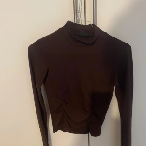 Brun långärmad topp från Gina Tricot - Säljer en snygg brun långärmad topp från Gina Tricot i storlek XXS. Toppen har en tight passform och är perfekt för höst och vinter. Den är i nyskick och redo för nya äventyr! med detaljer vid midjan