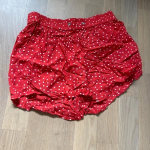 Röd prickig kjol i storlek XS - Säljer superfina shorts med vita prickar. Den har en elastisk midja med knappar för extra stil och komfort. Perfekt för sommarens alla fester eller bara en dag på stan. Kjolen är i ett lätt och luftigt material, vilket gör den idealisk för varma dagar.