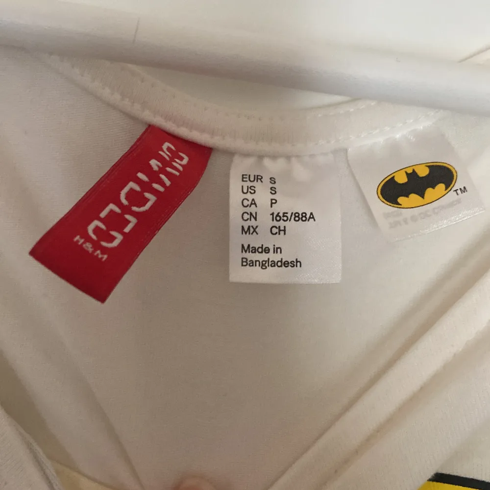 Säljer en supercool vit croppad topp från H&M med den ikoniska Batman-loggan i svart och gult på framsidan. Toppen har långa ärmar och är perfekt för en avslappnad och stilren look. Perfekt för alla Batman-fans!. Toppar.