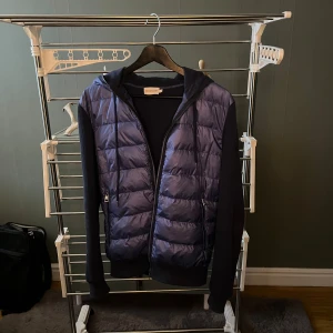 Blå pufferjacka från Moncler - Säljer en snygg blå cardigan från Moncler då jag vill testa nått nytt. Jackan har en snygg design med dragkedja och huva. Perfekt för kyliga sommar kvällar och hösten och ger en stilren look. Den är i storlek L. Kan gå ner i pris vid snabbaffär