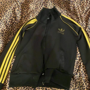 Svart och gul jacka från Adidas - super fin svart/guldig adidas jacka, andvänd mycket,dragkedja går inte att stänga men om man är händig går det säkert att lösa, emo,drainer,y2k💗 ganska liten i storleken men sjukt snygg tajt💗