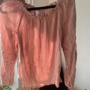Rosa blus med broderade detaljer - Säljer en söt rosa blus med långa ärmar och fina broderade detaljer på ärmarna. Blusen har en lös passform och en elastisk halsringning som ger en bekväm och avslappnad stil. Perfekt för vår och sommar!