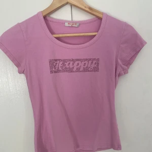 T-shirt  - Säljer denna rosa t-shirten med glittriga strassdetaljer på framsidan. Stretchigt material. Står M/L på tröjan men sitter som S. Trycket är lite slitet men annars bra skick. 