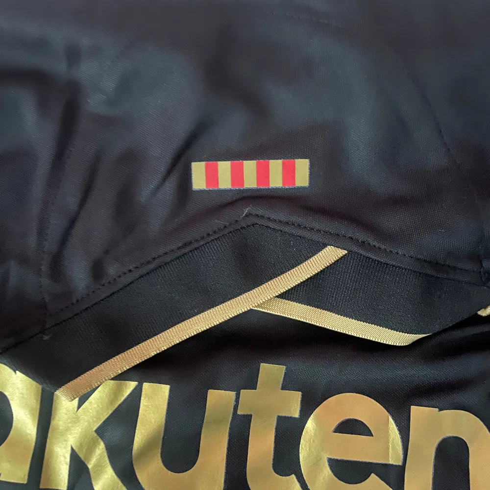 Säljer en snygg FC Barcelona tröja i svart med guldiga detaljer. Tröjan har korta ärmar och är i nyskick. Den har klubbens emblem och sponsorlogga i guld på framsidan. Perfekt för alla Barca-fans!. T-shirts.