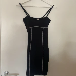 Svart klänning från H&M Divided - Säljer en stilren svart klänning från H&M Divided i storlek XS. Klänningen är ärmlös med smala axelband och har en tight passform. Den har dekorativa sömmar som ger en snygg detalj. Perfekt för fest eller en utekväll!