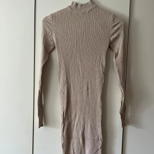 Beige ribbad klänning från Amisu - Säljer en superfin beige ribbad klänning från Amisu. Den är långärmad och har en tight passform som verkligen framhäver figuren. Perfekt för höst och vinter, och kan stylas både upp och ner beroende på tillfälle. Klänningen är i nyskick och redo för en ny garderob!