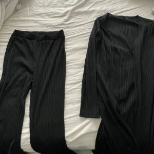 Svart ribbad klänning - Säljer ett svart ribbat set. Utvängda byxor och en lång cardigan med slits på sidorna. Använda 1 gång. båda för 200