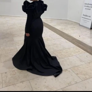 Svart festklänning  - Klänning i med hög slits, med öppen rygg och dramatiska axlar 