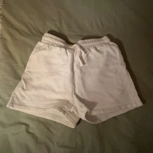 Vita shorts i bomull - Säljer ett par vita shorts i bomull. De har en elastisk midja för en bekväm passform. Perfekta för en avslappnad dag hemma eller en promenad i parken. Observera att det finns en liten fläck på framsidan.