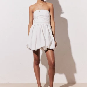 Vit kläning/ Studentklänning  - Snygg vit axelbandslös klänning med en luftig kjol och smockad rygg. Perfekt för varma sommardagar och festliga tillfällen. Är helt ny, prislappen är kvar kom privat för fler bilder. 