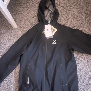 Svart Gore-Tex jacka från Haglöfs - Säljer en svart Gore-Tex jacka från Haglöfs, modell Chaos GTX. Jackan är vattentät och har en justerbar huva. Perfekt för utomhusaktiviteter och håller dig torr i alla väder. Även justerbara armar där nere och det längst ner på jackan, köpte för att jag skulle åka skidor men resan blev inte av så den är adelig andvänd