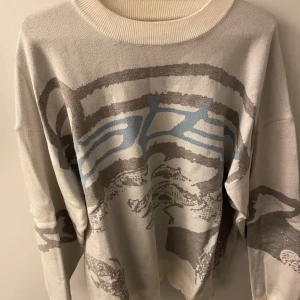 Beige och grå tröja med abstrakt mönster - Snygg beige tröja med abstrakt mönster i grått och blått. Tröjan har långa ärmar och en rund halsringning. Perfekt för en stilren look.