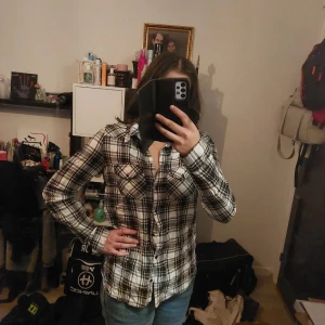 Rutig skjorta - Säljer en snygg rutig skjorta i svart och vit med långa ärmar och knappar framtill. Perfekt för en avslappnad stil.