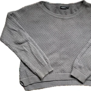 Grå stickad tröja från KappAhl - Mysig grå stickad tröja från KappAhl i storlek S. Tröjan har en rund halsringning och långa ärmar med ribbade muddar. Perfekt för kyliga dagar!