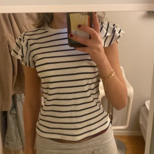 Randig topp med volangärmar - Säljer en söt randig topp med volangärmar. Toppen är vit med blåa ränder och har en ribbad struktur. Perfekt sen till sommarn me en vit kjol eller bara till jeans💕