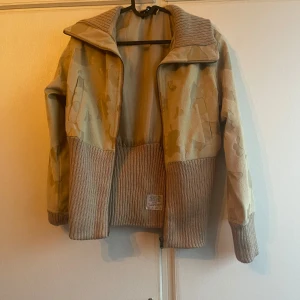 Beige camouflagemönstrad jacka från Farewell - Säljer en unik beige camouflagemönstrad jacka från Farewell. Jackan har en cool kombination av material med ribbade detaljer och dragkedja framtill. Perfekt för dig som vill sticka ut med stil.