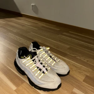 Nike sneakers med gul detalj  - Snygga Nike sneakers i vitt med svarta och gula detaljer. Skorna har en unik design med snörning och en bekväm sula. Perfekta för en sportig look. Storlek 42