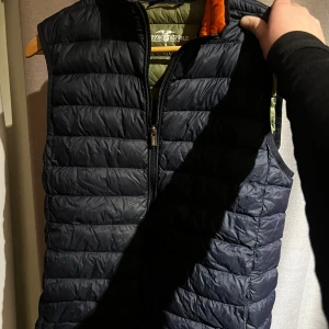 Mörkblå Grisch Dunväst, Hampton Republic - Säljer en stilren mörkblå dunväst från Hampton Republic. Västen har en dragkedja framtill och är i storlek S. Den passar perfekt som sommar och vårdagar där man vill vara varm stilig och lite grisch. 120kr. Dunderpris!! Jag har använt den även fast jag var medium