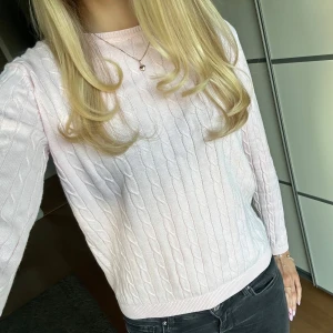 Ljusrosa stickad tröja  - Säljer en ljusrosa stickad tröja med kabelstickat mönster. Tröjan har långa ärmar och en rund halsringning. 