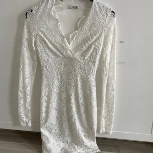 Vit spetsklänning från Nelly  - En jätte vacker vit spetsklänning från Nelly med v-ringad design och långa ärmar. Perfekt för speciella tillfällen med sin fina spetsdetalj och figurnära passform. Använd en gång! Klänningen har två små sminkfläckar som man ser på sista bilderna men ska tvätta den o se om det går bort!💕annars är det inget man märker eftersom en av de är på insidan o den andra är så liten. Pris kan diskuteras 