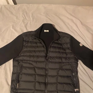 Moncler cardigan svart - Snygg svart pufferjacka från Moncler med dragkedja och långa ärmar. Jackan har ett quiltat mönster på framsidan och en broderad logotyp på ärmen. Perfekt för kyligare dagar. Använd ett par gånger men har inga skador alls, letar ny jacka så säljer denna till ett bra pris. Storlek M och kan passa S. Men skulle mer säga personer med storlek M som jag. Priset kan diskuteras vid snabbaffär