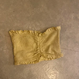 Gul tubtopp från Bik Bok - Säljer en söt gul tubtopp från Bik Bok med volangdetaljer upptill och nedtill. Toppen är elastisk och perfekt för sommardagar. Passar bra till både kjol och jeans.