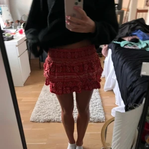 Röd mönstrad kortkjol - Trendig röd kortkjol med volanger och ett snyggt mönster. Perfekt för att ge en färgklick till din outfit. Kjolen har en omlott-design som ger en extra touch av stil.