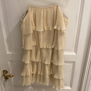 Gul klänning med volanger - Elegant beige offshoulder klänning med flera lager av volanger. Perfekt för en somrig look med sin luftiga och lätta design. Använd 1 gång