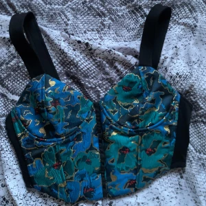 Korsettopp från Zara - Snygg blommig korsettopp från Zara i gröna och blå nyanser med svarta axelband, finns även sjukt fina guld detaljer. Finns även korsett krokar på framsidan om man hakar av och på för att sätta på sig den. Toppen har en v-ringad design och är perfekt för en trendig look. Sjukt bra att ha om man behöver en snygg topp till en fest! Är i nyskick☺️❤️