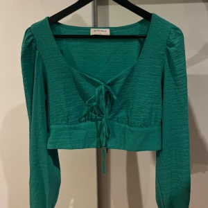 Grön topp från Rut&circle - Snygg grön topp från Eut&Circle med knytning framtill. Toppen är croppad och har långa ärmar, perfekt för en trendig look.