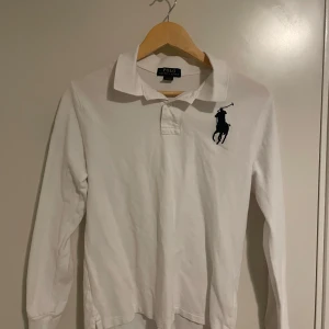 Polo Ralph Lauren - Säljer en klassisk vit långärmad pikétröja från Polo Ralph Lauren. Tröjan har en broderad logga på bröstet och en stor siffra '3' på ärmen. Perfekt för en stilren och sportig look. Först behöver tjäna pengar för nya skor. Priset går att diskutera vid snabb affär 