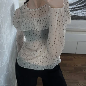 Blus - Säljer en söt vit blus med svarta prickar och volangdetaljer. Blusen har långa ärmar och en luftig passform, perfekt för både vardag och festliga tillfällen😄 Aldrig använd!