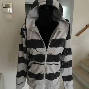 Randig hoodie med dragkedja - Säljer en cool randig hoodie i svart och vit med dragkedja framtill. Perfekt för en avslappnad stil med sin bekväma passform och huva. Passar bra till jeans eller joggers för en casual look.