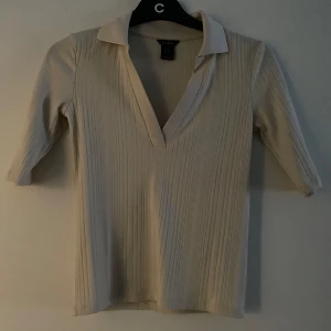 Beige ribbad tröja med krage - Snygg beige ribbad tröja med krage och v-ringning. Tröjan har trekvartsärmar och en stilren design 