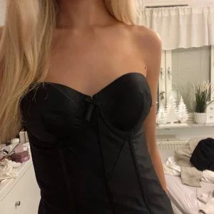 Svart korsett - Snygg svart korsett med avtagbara axelband och en liten rosett framtill. Perfekt för en stilren och elegant look. Passar bra till både jeans och kjol. Korsetttopp . Skulle säga att den är 75B men även en C skulle passa.