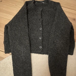 Mörkgrå kofta med knappar - Säljer en mysig mörkgrå kofta med knappar framtill. Perfekt för kyliga dagar med sin varma och bekväma design. Koftan har långa ärmar och en klassisk stil som passar till det mesta.