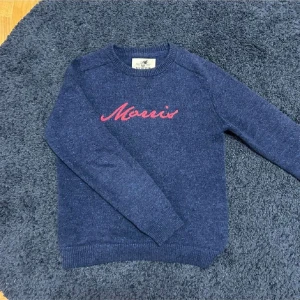 Blå stickad tröja från Morris - Säljer en snygg blå stickad tröja från Morris med röd broderad text på bröstet. Tröjan har långa ärmar och ribbstickade muddar vid ärmslut och nederkant. Perfekt för kyliga dagar! Tröjan är köpt från morris för 2699, den är gjord av kashmir, priset är inte hugget i sten