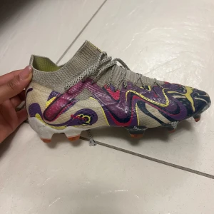 Färgglada fotbollsskor med mönster - Snygga fotbollsskor med ett unikt, färgglatt mönster i lila, gul och beige. Skorna har snörning och en strumpliknande passform för extra komfort på planen.