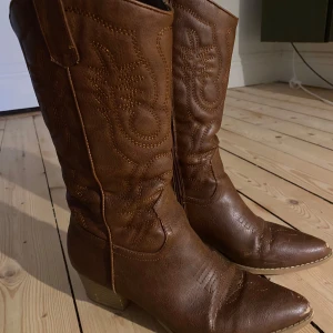 Bruna cowboy boots med broderad detalj - Snygga bruna cowboy boots i skinn med broderade detaljer. De har en spetsig tå och en låg. Det slitna syns på bilderna.