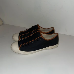 Svarta sneakers från Polo Ralph Lauren - Svarta sneakers från Polo Ralph Lauren med bruna detaljer och snörning. Sulan är lite smutsig men bör enkelt gå att tvätta bort. Storlek 10,5 vilket motsvarar storlek 44!                        Pris kan diskuteras vid snabb affär!!