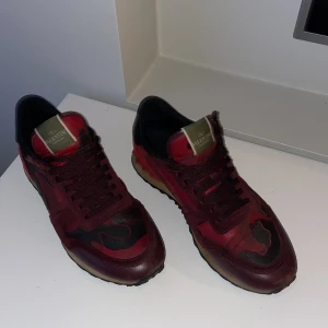 Valentino Rockrunner sneakers i rött och svart - Snygga Valentino Rockrunner sneakers i en djärv kombination av rött och svart. Skorna har en unik design med svarta detaljer och en robust sula. De är tillverkade i en mix av skinn och mocka, vilket ger en lyxig känsla. Perfekta för den som vill sticka ut med stil. Storlek 43 obs de blöta på skorna är endast vatten. Skriv vid minsta fråga eller fundering. Säljer för att dom är för stora. Dust bag finns inte på bilderna med de får man självklart med. Kan gå ner i pris vid snabb affär.