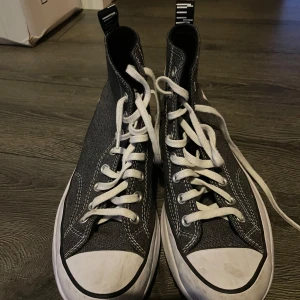 Svarta höga sneakers från Converse - Säljer ett par svarta höga sneakers från Converse med vit sula och vita snören. Skorna har en klassisk design med rund tå och märkets logga på sidan. Perfekta för en casual look.