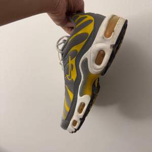 Säljer ett par Nike sneakers i grått och gult med snörning. Skorna har en unik design med synliga luftkuddar i sulan för extra komfort. Perfekta för en sportig look.