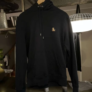 Blå hoodie från Maison Kitsuné - Säljer en stilren svart hoodie från Maison Kitsuné med en söt broderad rävdetalj på bröstet. Tröjan har en klassisk design med dragsko i huvan och en stor ficka framtill. Perfekt för en avslappnad look. Skicket är perfekt. Storlek S men passar M. För fler frågor eller bilder kom privat. Priset är ej hugget i sten!
