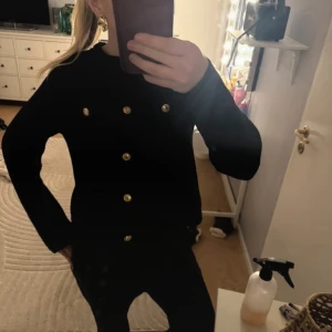 Svart kofta från H&M - Säljer en snygg svart kofta från H&M med dekorativa knappar i silver. Koftan har en texturerad yta och långa ärmar, perfekt för kyligare dagar. Den har en klassisk rund halsringning och ribbade kanter.❤️