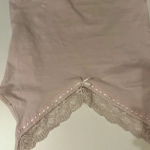 Rosa linne från Gina Tricot - Säljer ett sött rosa linne från Gina Tricot med spetsdetaljer och en liten rosett framtill. Perfekt för en feminin och romantisk look.